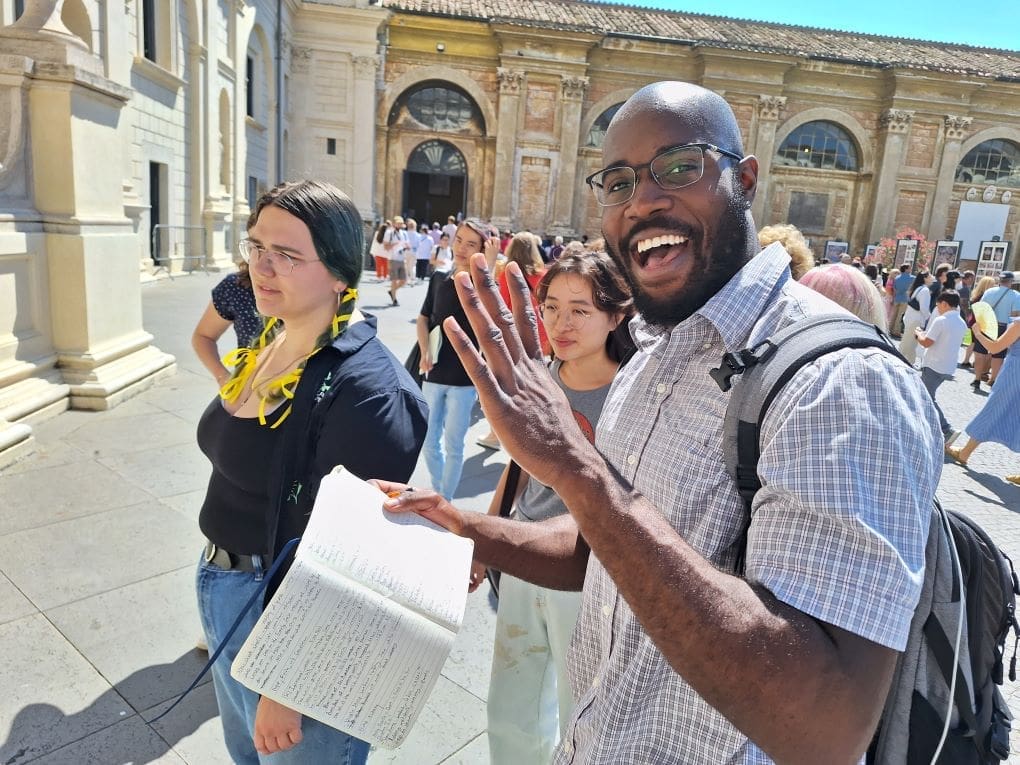 student smiling with a book in front of the Vatican museum, with a crowd