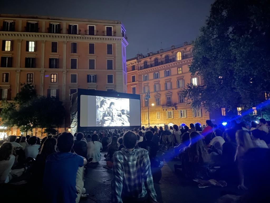a crowd in the dark in front of a movie projected outdoors