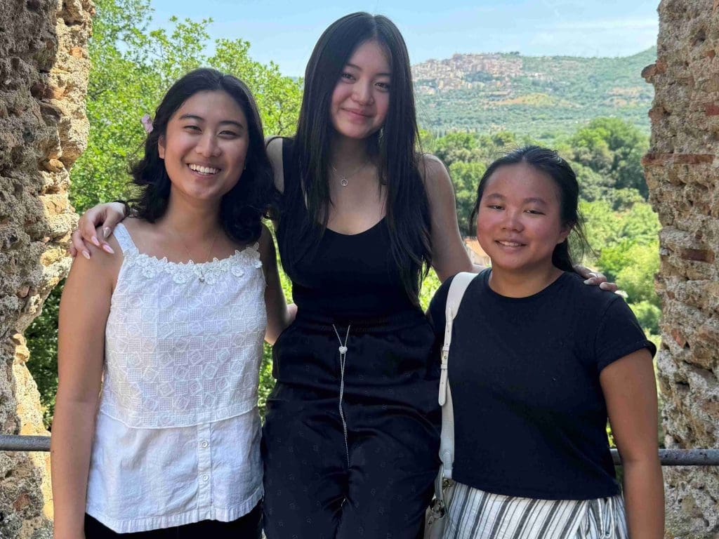 three students at Hadrian's villa in Tivoli, standing at a railing with Italian trees, brush, and desert hills behind them