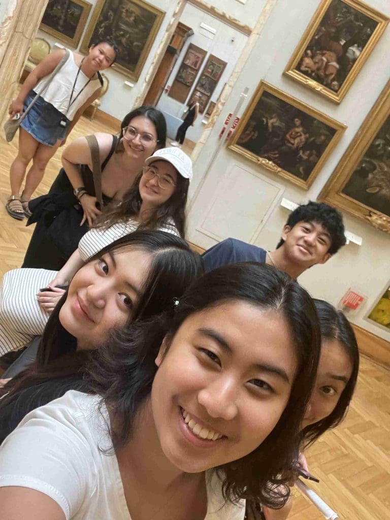 a group selfie of seven students in a museum gallery with oil paintings in the background